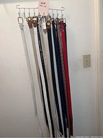 Ten belts hung on a rack, showing full length and variety of styles and colors.