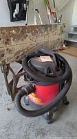 Side view of the wet/dry vacuum and folding workbench showing the vacuum hose wrapped around the vacuum, and the worn wooden bench top.