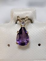 Front view of the 10K gold pendant showing the pear-shaped purple amethyst and round accent stone above it on a white textured display card.