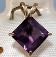 Close-up front view of square-cut amethyst in gold prong setting.