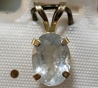 Close-up image of the aquamarine pendant showing the oval faceted light blue stone secured by four yellow gold prongs.