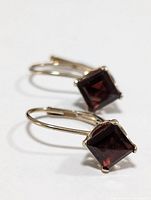 Pair of 14K gold earrings with square-cut dark red garnet gemstones shown from a side angle illustrating the lever-back clasp and stone setting.
