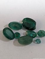 Photo showing 8 genuine emerald gemstones in various sizes and cuts on a plain surface for detail and color evaluation.