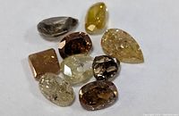 Nine loose faceted diamonds arranged on white surface showing various cuts and colors