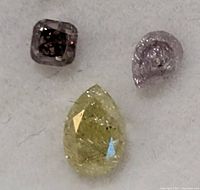 Close-up of three diamonds showing colors and shapes: yellow pear, light pink pear, dark gray cushion cut.