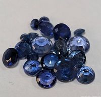 Close-up of multiple loose blue faceted sapphires of varying sizes on white background.