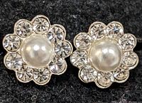 Close-up of the front side of silver-colored flower earrings showing central faux pearl surrounded by clear crystals