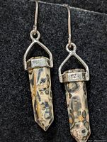 Pair of silver earrings with natural stone pendants on black fabric background, showing front detail and pattern of stones.