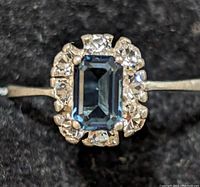 Close-up photo of the silver ring showcasing the rectangular blue central stone surrounded by clear stones on a black background.