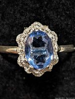 Front close-up view of the silver ring showing the faceted blue oval gemstone and ornate silver setting.