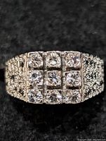 Close-up photo of the front face of a silver ring showing 9 clear round-cut stones in a square pattern.