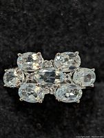 Close-up front view of sterling silver ring with seven oval blue topaz stones arranged in a three-row cluster on a black background.