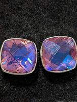 Close-up photo of cushion-cut mystic quartz earrings showing pink and blue color reflections on a black background.