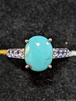Close-up photo showing oval turquoise cabochon center stone and tanzanite accent stones on the band in sterling silver setting.