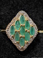 Close-up front view of sterling silver ring with emerald cluster and white pavé stones.