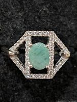 Front view showing oval green emerald in the center, surrounded by two sparkling rectangular frames of small clear stones set in sterling silver.