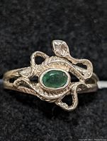 Close-up front view of sterling silver snake ring with central oval green emerald.