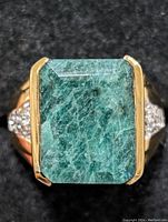 Front view showing large rectangular emerald set with gold-tone prongs and small clear stones on ring sides.