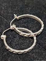 Pair of sterling silver hoop earrings with faceted texture, shown flat on black background