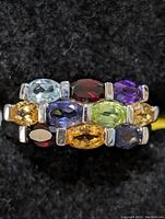 Close-up top view of silver ring showing oval and marquise cut multi-colored gemstones set in three horizontal rows.