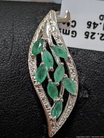 Close-up front view of the sterling silver pendant showing the emerald stones and decorative white stones on the edge.