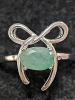 Close-up front view of sterling silver ring with oval green emerald gemstone and infinity-style design.