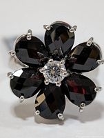 Front view image showing flower-shaped cluster of six deep red garnet stones with clear stone centerpiece, set in polished sterling silver ring.