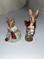 Front view of two Beswick Bunnykins porcelain rabbit figurines, one knitting, one on rocking horse.