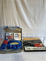 Photo shows Kreg Deck Jig parts including plastic jig with metal drill guide holes, multiple red and blue spacers, instructional DVD and quick-start guide inside gray plastic case.