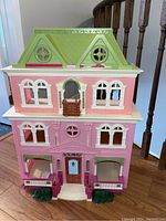 Front view of the pink and green Fisher Loving Family Dollhouse showing three floors, six windows, blue door, two balconies with purple shutters, and detailed trim.