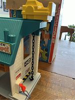 Front-side view showing teal roof, yellow elevator mechanism, black chain lift, and orange crane arm with hook.