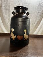 Front view of black metal milk can showing hand painted ducks, hearts, and 'WELCOME FRIENDS' lettering.