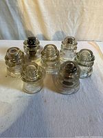 Seven vintage clear glass hydro insulators arranged in two rows on a white cloth background.