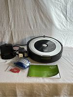 Roomba vacuum with charging base, power adapter, cleaning tool, filter, and owner's guide arranged on table.