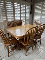 Full view of the oak dining table seated with 6 chairs in a bright room with white shuttered windows.
