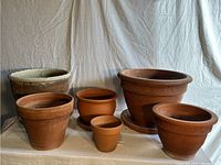 Front view of six terra cotta planters of various sizes on a white cloth background