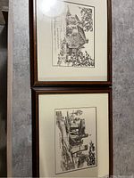 Two framed black and white architectural prints hung on a wall, showing buildings and trees in simple wood frames.