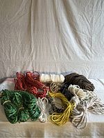 Photo of various ropes of differing colors and thicknesses arranged on a flat surface with a white cloth background.