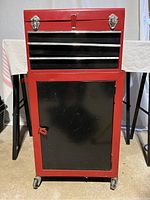 Full view of the tool chest and storage box on caster wheels showing red upper chest with black drawer section and black bottom cabinet with door.