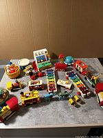 Overview photo of all vintage Fisher Price toys including music box, cash register, train, pull toys, and figures on table