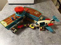 Full view of vintage Fisher-Price airport playset including terminal with control tower, airplane, small car, wooden figures, and freight train cars.