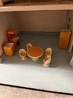 Dollhouse kitchen and dining room with orange and yellow vintage Fisher Price furniture, including round table, chairs, stove, sink, and refrigerator.