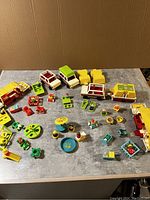 Photo showing entire assortment of vintage Fisher Price Little People pop-up campers, vehicles, playground equipment, and figures spread on a table.