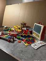 Wide view of all vintage Fisher Price toys arranged on a table against a cardboard backdrop.