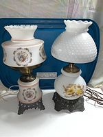 Full front view of both vintage lamps showing their glass and metal bases with floral decorations.
