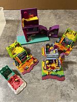 Purple two-story Polly Pocket house open showing interior with furniture plus five Polly Pocket compact playsets with detailed interiors spread on floor