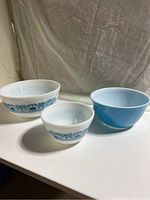 Three vintage Pyrex mixing bowls displayed side by side on a white surface. Shows different sizes and patterns.