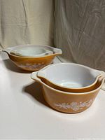 Four nested vintage Pyrex casserole dishes with orange exterior and white floral pattern, interior and handles visible.