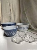 Six mixing bowls displayed including three blue and white Pyrex bowls with floral Colonial Mist pattern and three clear glass bowls