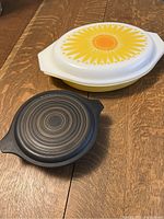 Two vintage Pyrex casserole dishes with lid, showing Crazy Daisy and Terra patterns, placed on a wooden table.